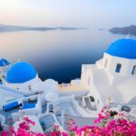 Discovering Santorini: A Journey Through Greece’s Most Iconic Island A breathtaking view of Santorini’s whitewashed houses with blue domes overlooking the Aegean Sea at sunset.